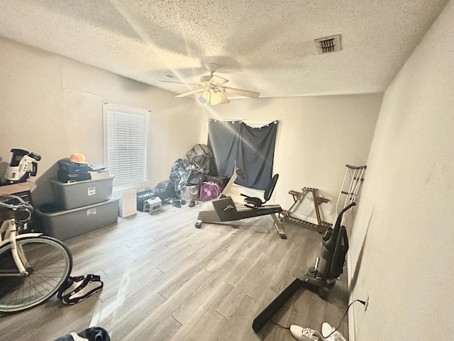 exercise area featuring ceiling fan, wood-type flooring, and a textured ceiling