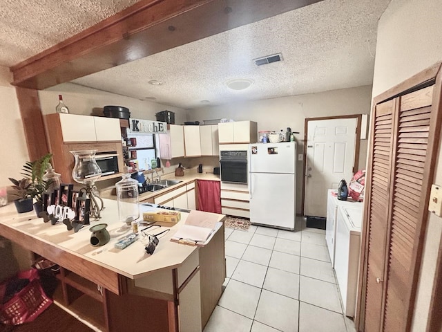 kitchen with light tile patterned flooring, washer and dryer, kitchen peninsula, black oven, and white fridge