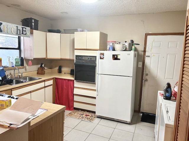 kitchen featuring sink, black oven, white refrigerator, a textured ceiling, and light tile patterned flooring