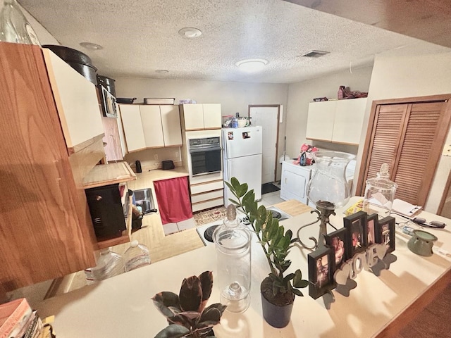 kitchen featuring a textured ceiling, black oven, white fridge, and white cabinets