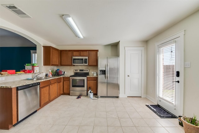 kitchen with sink, appliances with stainless steel finishes, light stone countertops, light tile patterned flooring, and decorative backsplash