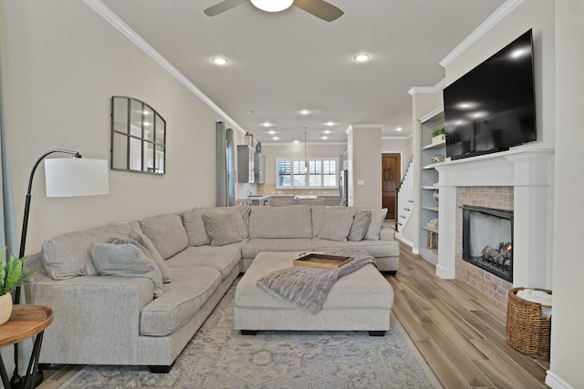 living room featuring crown molding, ceiling fan, a fireplace, and light hardwood / wood-style flooring