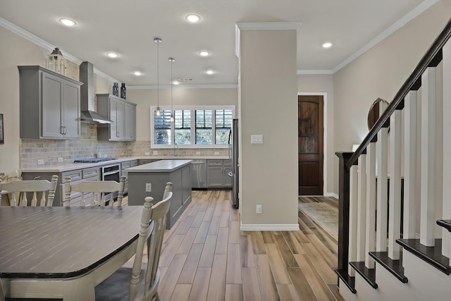 kitchen with wall chimney range hood, gray cabinets, hanging light fixtures, stainless steel appliances, and a center island