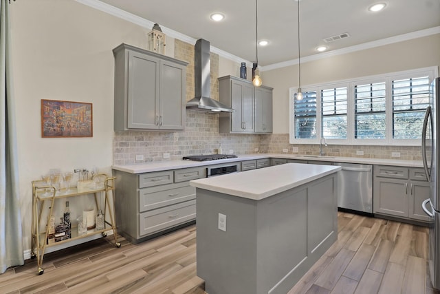 kitchen with wall chimney range hood, sink, appliances with stainless steel finishes, light hardwood / wood-style floors, and a kitchen island