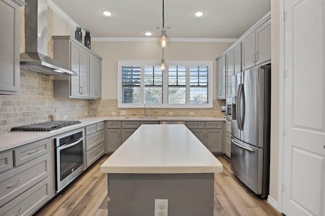 kitchen featuring gray cabinetry, appliances with stainless steel finishes, a kitchen island, and wall chimney range hood