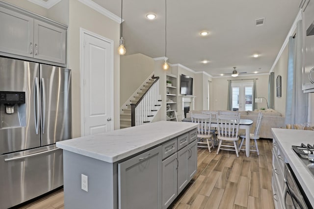 kitchen with stainless steel refrigerator with ice dispenser, decorative light fixtures, light hardwood / wood-style flooring, gray cabinets, and a kitchen island