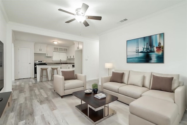 living room with sink, crown molding, light hardwood / wood-style flooring, and ceiling fan