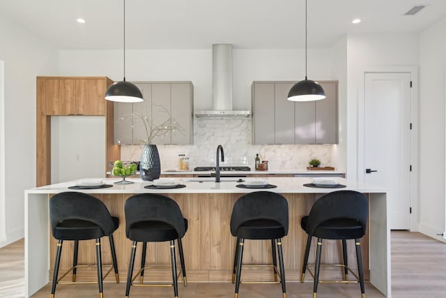 kitchen with tasteful backsplash, an island with sink, wall chimney exhaust hood, and a breakfast bar