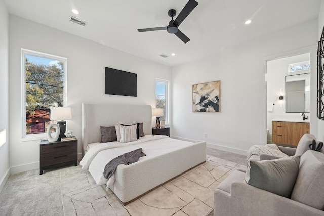 bedroom with ceiling fan, light colored carpet, and ensuite bath