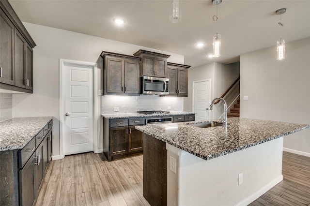 kitchen featuring appliances with stainless steel finishes, pendant lighting, sink, dark stone countertops, and dark brown cabinets