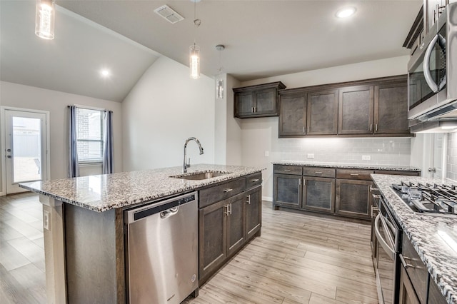 kitchen with lofted ceiling, sink, a kitchen island with sink, stainless steel appliances, and decorative light fixtures