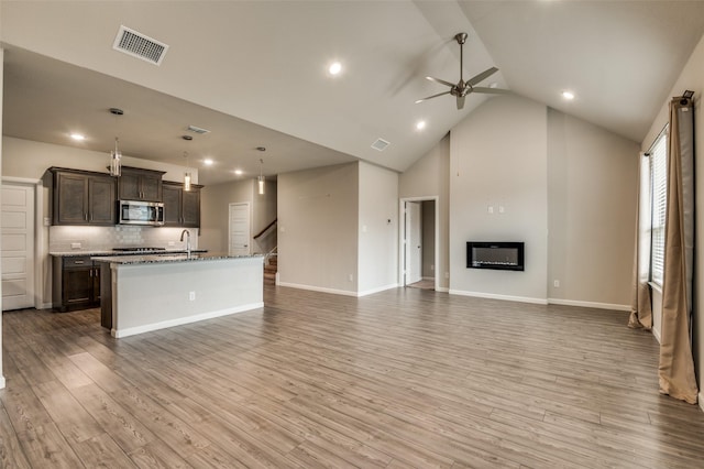 kitchen with tasteful backsplash, dark brown cabinetry, light hardwood / wood-style floors, and a center island with sink