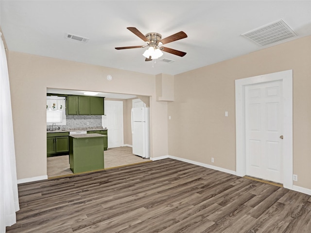 kitchen with dark wood-type flooring, sink, green cabinets, white fridge, and decorative backsplash