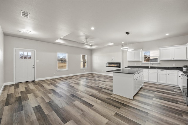 kitchen with dark hardwood / wood-style floors, decorative light fixtures, white cabinetry, sink, and a tray ceiling