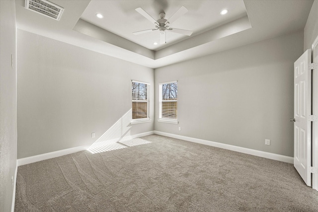 carpeted spare room with a raised ceiling and ceiling fan