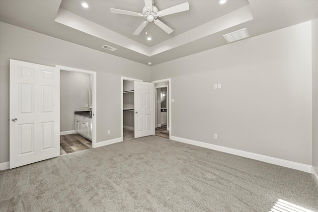 unfurnished bedroom with ceiling fan, carpet, connected bathroom, a spacious closet, and a raised ceiling