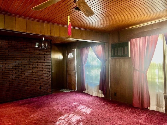 unfurnished room with ceiling fan, carpet flooring, and wood walls