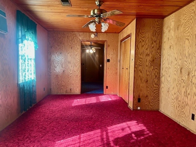 carpeted spare room with wooden ceiling, ceiling fan, and wood walls