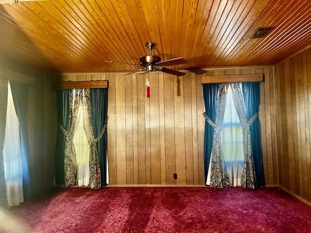 unfurnished room with wooden walls, ceiling fan, and carpet flooring