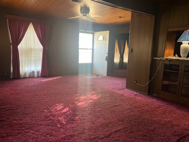 carpeted empty room with ceiling fan and wood walls