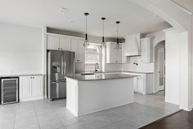 kitchen featuring tasteful backsplash, white cabinetry, wine cooler, a center island, and stainless steel refrigerator with ice dispenser