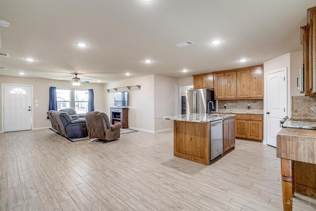 kitchen featuring stainless steel appliances, light stone countertops, light hardwood / wood-style flooring, and backsplash