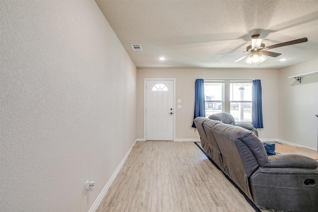 living room featuring ceiling fan, a textured ceiling, and light wood-type flooring