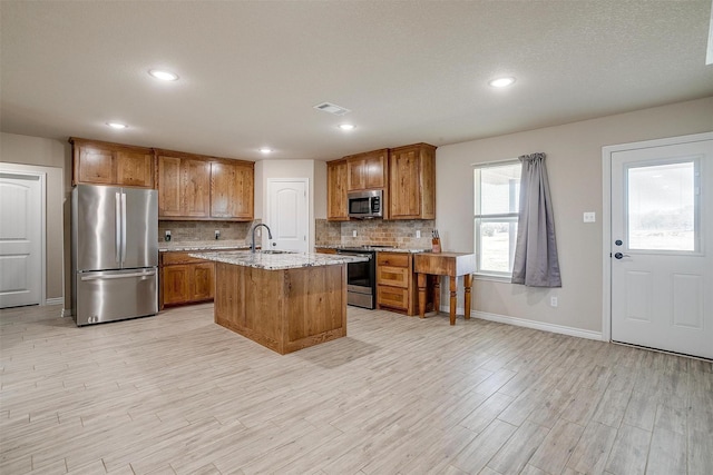 kitchen featuring appliances with stainless steel finishes, tasteful backsplash, sink, a kitchen island with sink, and light stone counters