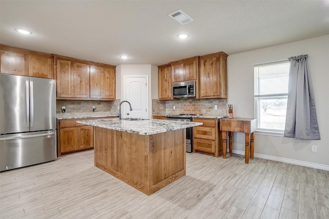 kitchen with appliances with stainless steel finishes, tasteful backsplash, sink, light stone countertops, and a center island with sink