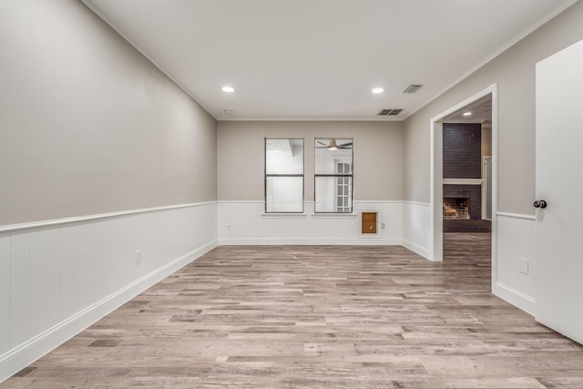 spare room featuring a brick fireplace, crown molding, and light wood-type flooring