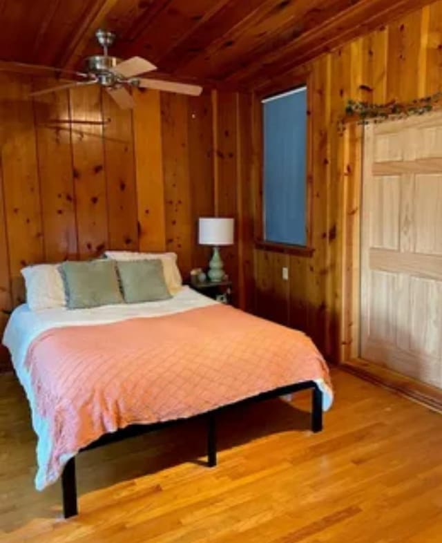 bedroom featuring hardwood / wood-style floors, wood ceiling, wooden walls, and ceiling fan