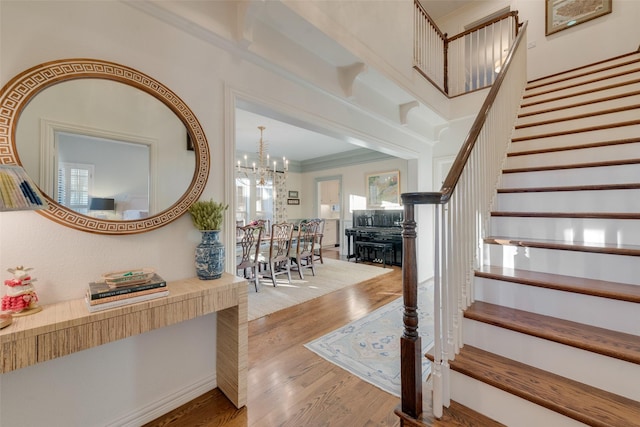 staircase featuring hardwood / wood-style flooring, ornamental molding, and a chandelier