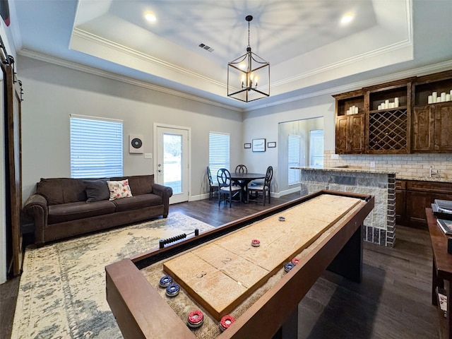 playroom with dark hardwood / wood-style flooring, ornamental molding, a raised ceiling, and an inviting chandelier