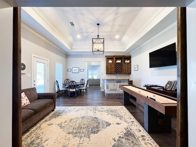 living room featuring an inviting chandelier, a tray ceiling, dark wood-type flooring, and indoor bar