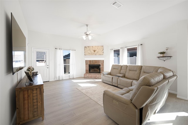 living room featuring vaulted ceiling, ceiling fan, a brick fireplace, and light hardwood / wood-style floors