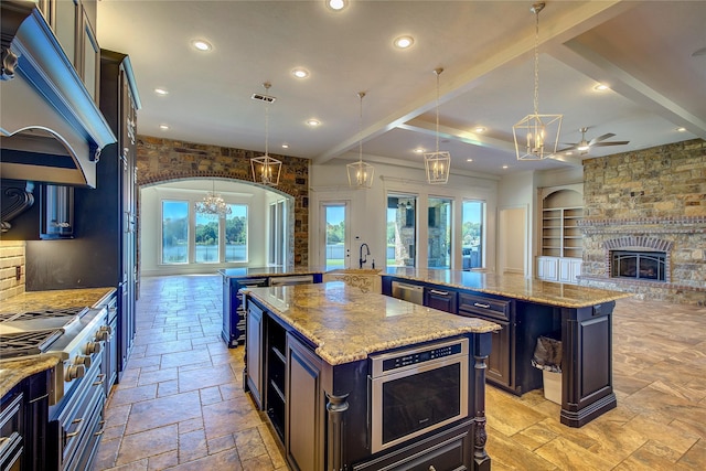 kitchen with hanging light fixtures, a brick fireplace, a center island with sink, and light stone counters