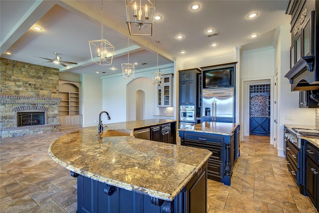 kitchen with built in features, appliances with stainless steel finishes, a spacious island, light stone counters, and decorative light fixtures