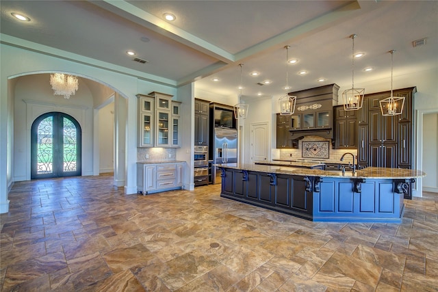 kitchen with tasteful backsplash, a spacious island, hanging light fixtures, light stone countertops, and french doors