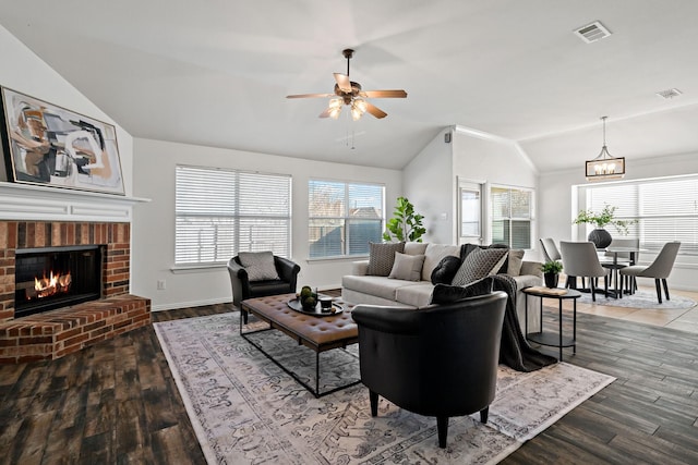 living room with a brick fireplace, a wealth of natural light, vaulted ceiling, and dark wood-type flooring