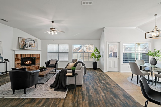 living room with a brick fireplace, ceiling fan with notable chandelier, vaulted ceiling, and light wood-type flooring