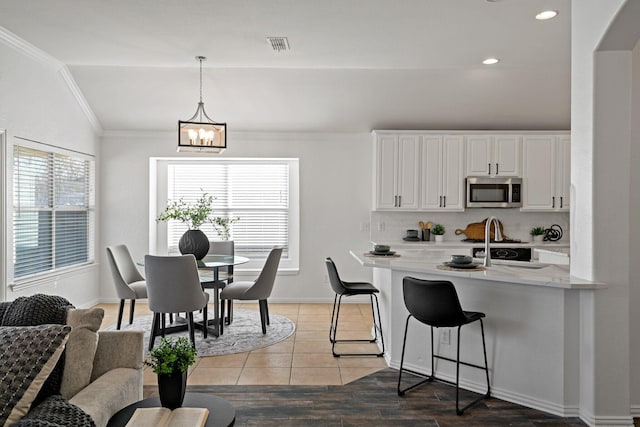 kitchen with range, hanging light fixtures, light stone counters, white cabinets, and vaulted ceiling