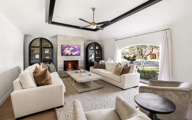 living room featuring ceiling fan, wood-type flooring, a tiled fireplace, and a raised ceiling