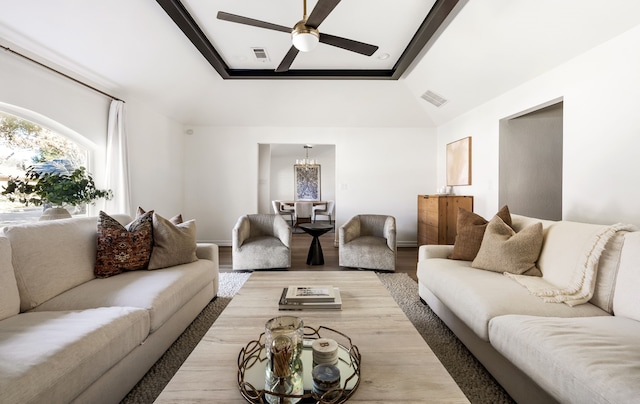 living room featuring lofted ceiling, wood-type flooring, a raised ceiling, and ceiling fan with notable chandelier