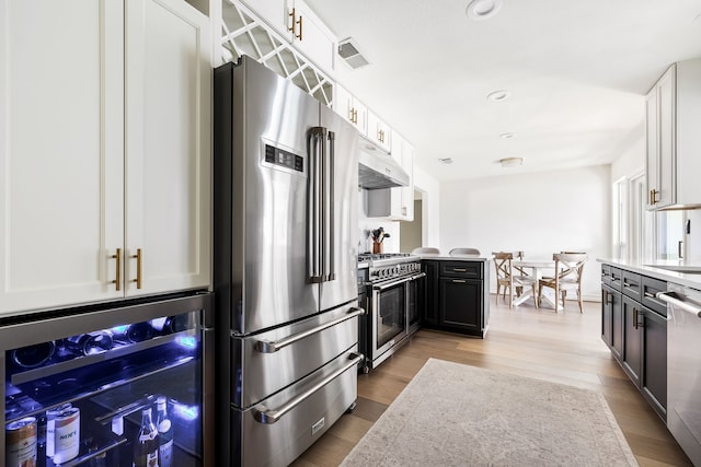 kitchen featuring high quality appliances, white cabinetry, beverage cooler, and light hardwood / wood-style flooring