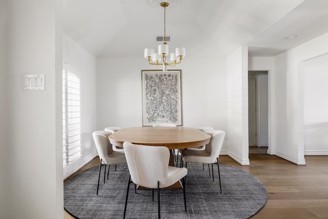 dining area with a notable chandelier, lofted ceiling, visible vents, wood finished floors, and baseboards