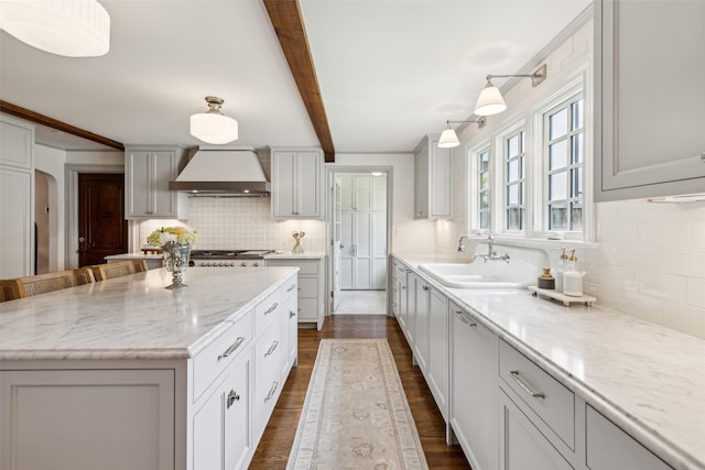 kitchen featuring a kitchen island, decorative light fixtures, beamed ceiling, a breakfast bar area, and custom exhaust hood