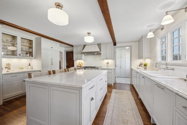 kitchen featuring a kitchen island, custom range hood, sink, and decorative light fixtures