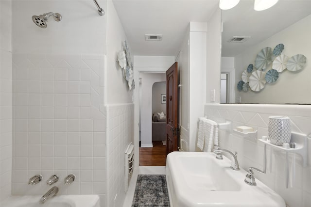 bathroom with tile walls, sink, heating unit, and washtub / shower combination