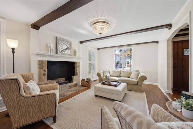 living room with beam ceiling, hardwood / wood-style floors, a stone fireplace, and ornamental molding