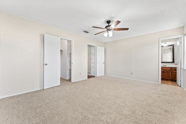 unfurnished bedroom with light carpet, connected bathroom, a walk in closet, and ceiling fan